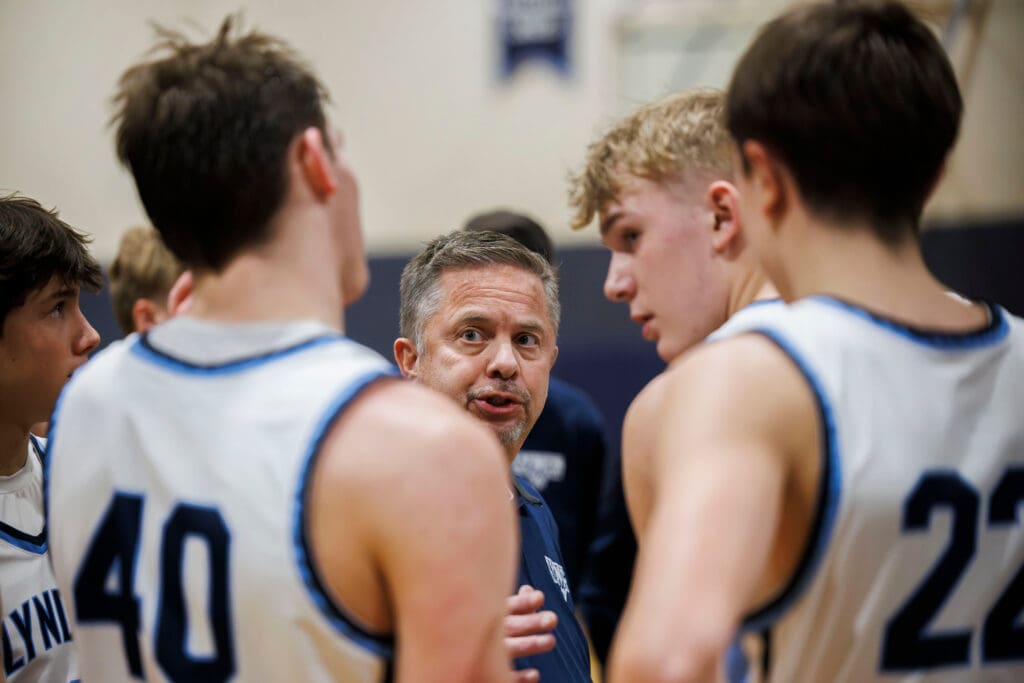 Lynden Christian head coach Tim Zylstra talks to his team during a timeout as he is surrounded in a huddle by his team.