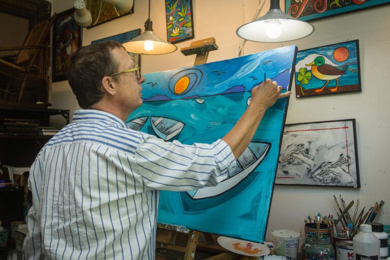 Inside Ben Mann Studios, Ben Mann paints a bright blue painting propped up by an easel.