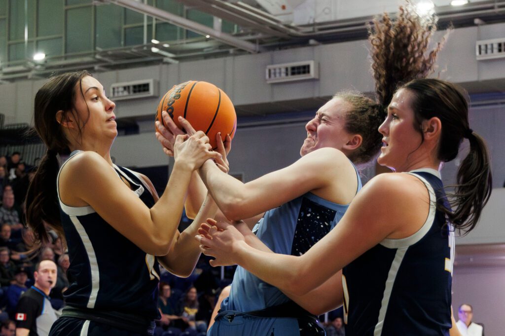 Western Washington University's Olivia Wikstrom fights for the ball against two opposing members, one of which grabs hold of her wrists.