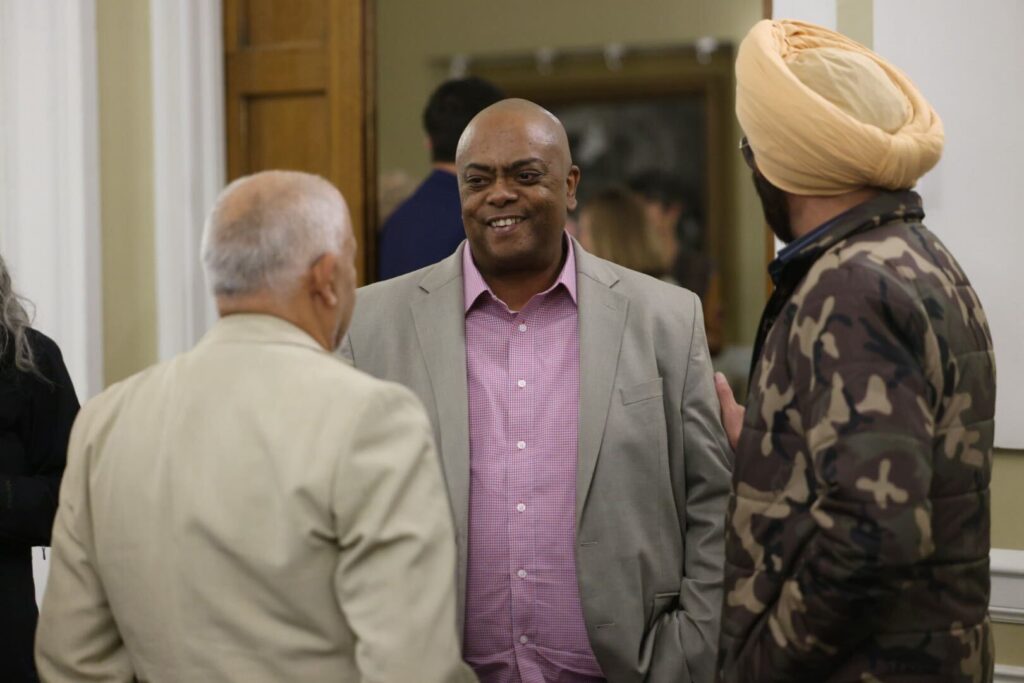 Whatcom County sheriff candidate Donnell "Tank" Tanksley talks to Surjit Singh, left, and Rashpal Sandhu, who's holding Tanksley's arm, in front of a large doorway.