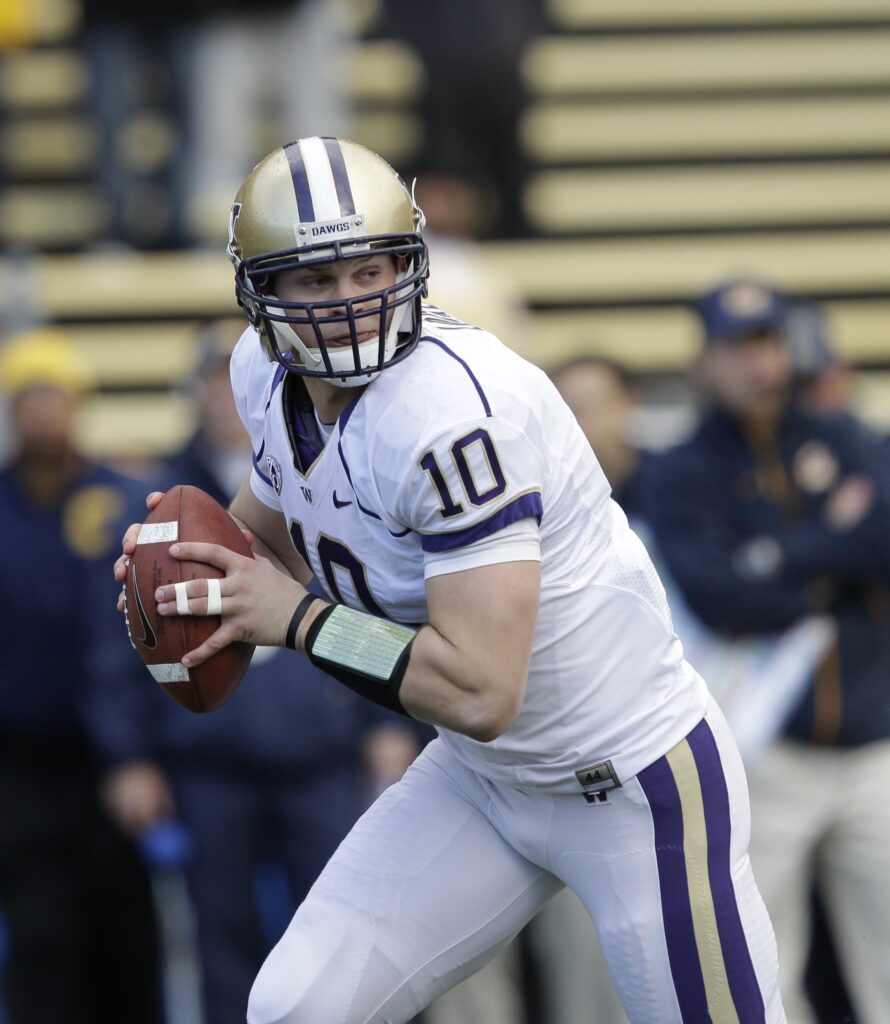 University of Washington quarterback Jake Locker rolls out and looks to pass as he holds the ball to his side while spectators watch from behind him.