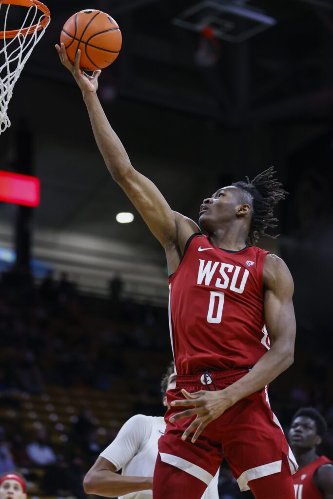 Washington State University forward Efe Abogidi (0) puts in a layup as he leaps into the air to reach the basket while other players watch in reaction.