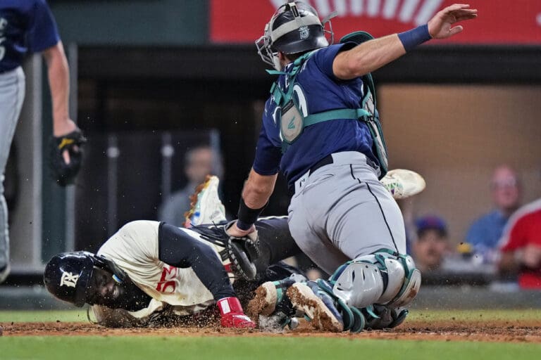 Texas Rangers' Adolis Garcia scores past Seattle Mariners catcher Cal Raleigh (29) during the fifth inning of a baseball game in Arlington