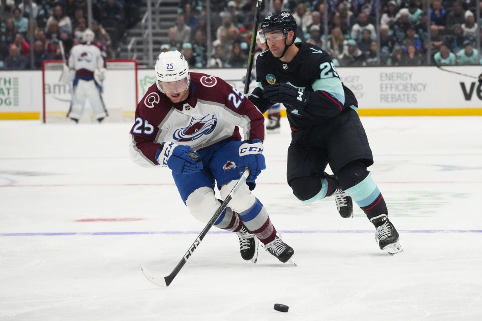 Colorado Avalanche right wing Logan O'Connor (25) breaks away from Seattle Kraken defenseman Vince Dunn (29) to chase after the ball as spectators and goalkeeper watch from afar.