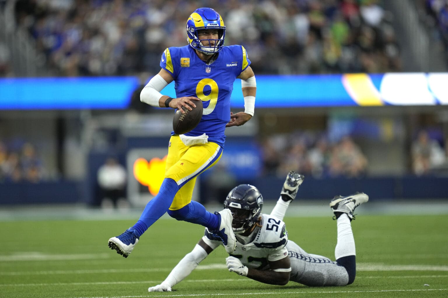 Los Angeles Rams quarterback Matthew Stafford (9) runs the ball after evading a tackle from a defender, leaving linebacker Darell Taylor on the grass.