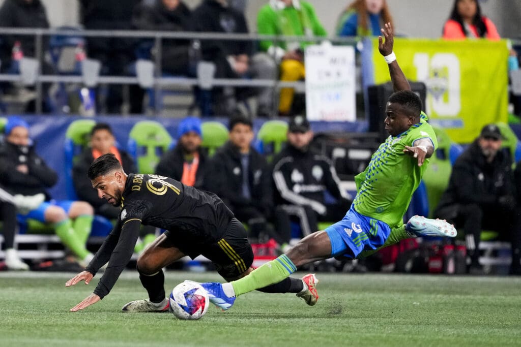 Seattle Sounders defender Nouhou Tolo reaches out with the tip of his foot as another player falls to the grass field.