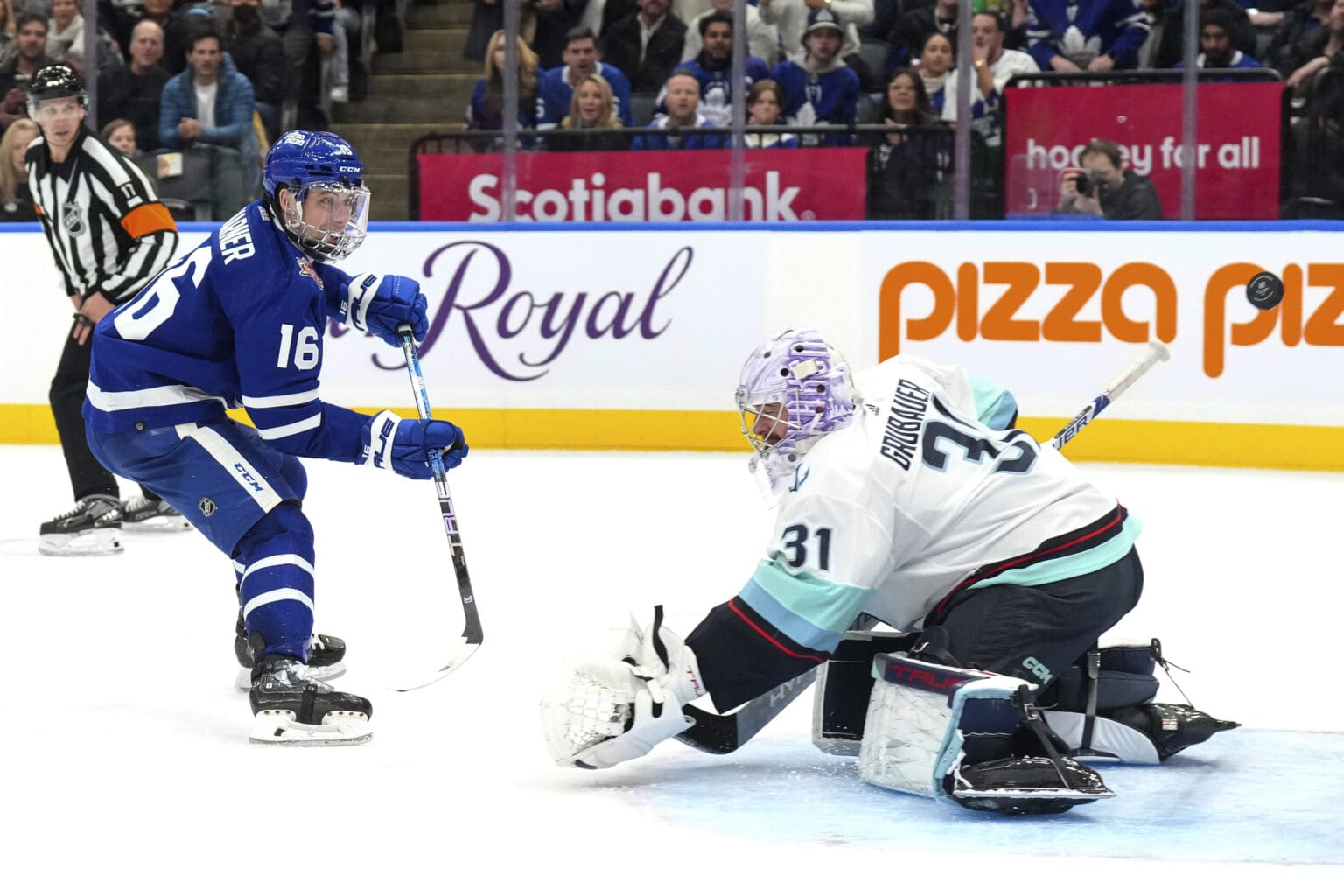 Toronto Maple Leafs' Mitchell Marner revs up his stick to take a shot as a goalie crouches to try and block.