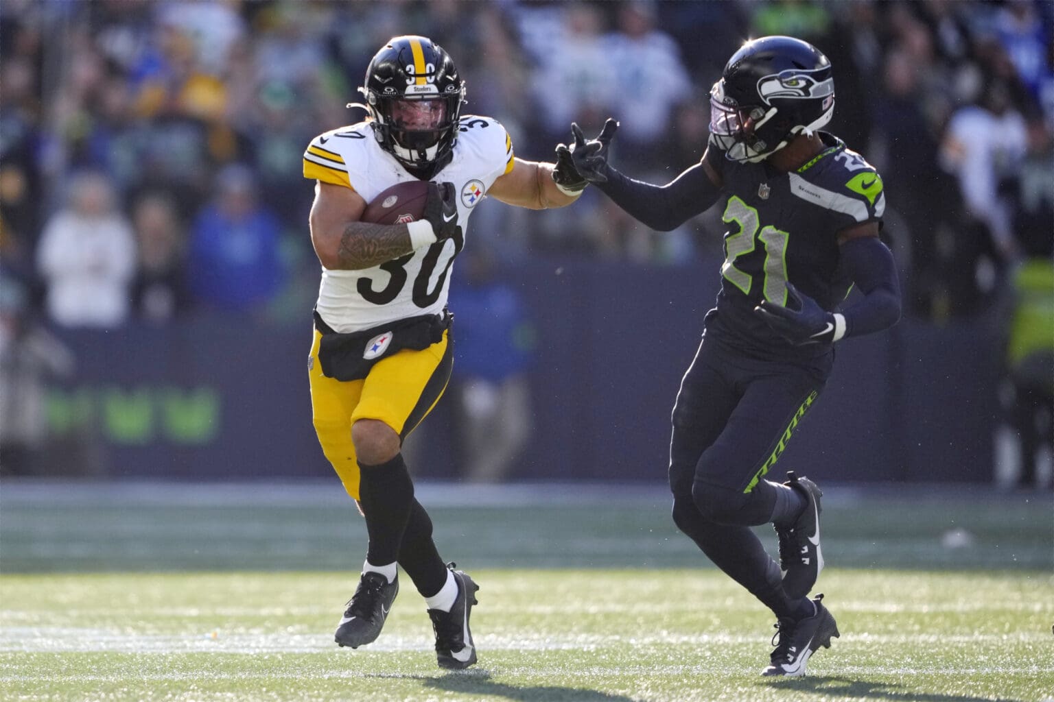 Pittsburgh Steelers running back Jaylen Warren (30) tries to get past Seattle Seahawks cornerback Devon Witherspoon (21) as he stretches out his arm to shove him away.