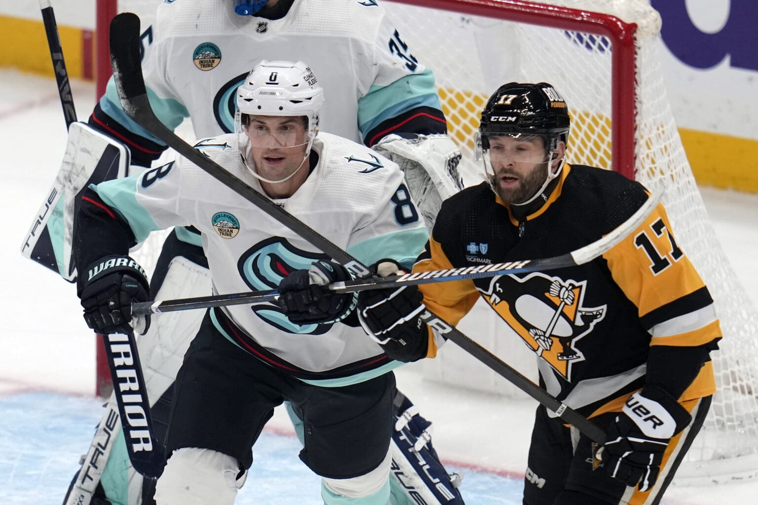 Seattle Kraken's Brian Dumoulin battles for control with Pittsburgh Penguins' Bryan Rust as their hockey sticks are tangled with each other.