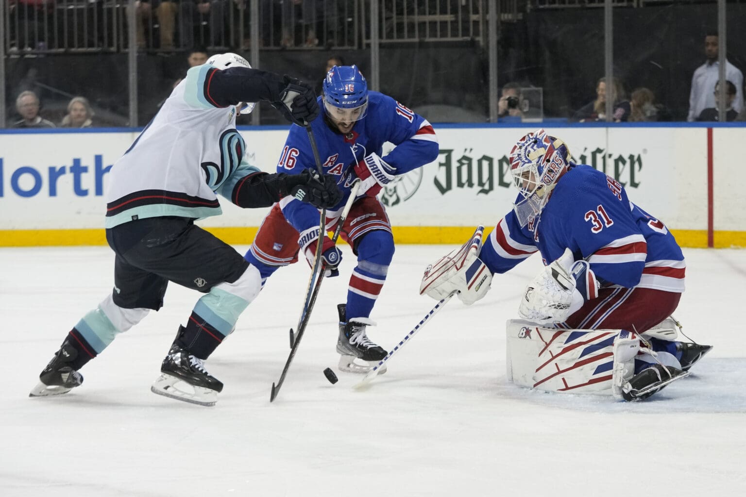 New York Rangers goaltender Igor Shesterkin leans to block the shot as two other players battle for control for the puck.
