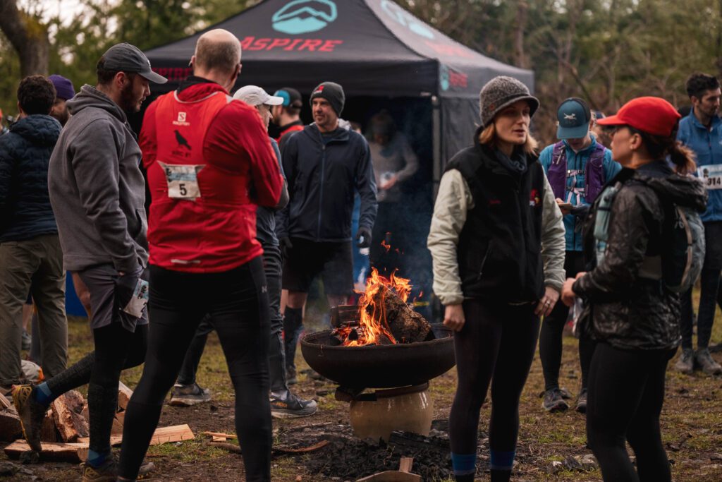 Runners gather near a fire as they get warm and chat amongst themselves.