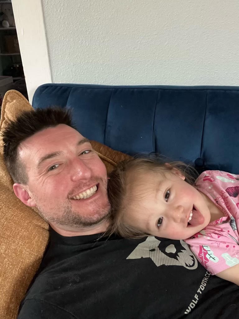 Restaurant owner Nathaniel "Nate" Breaux laying on a blue sofa with his daughter, Izabella.