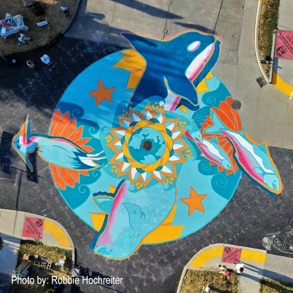 An aerial view of "A Hope Project Mural, 2023" at West North and Lynn Streets shows a colorful design of orcas, salmon, seals, and birds.