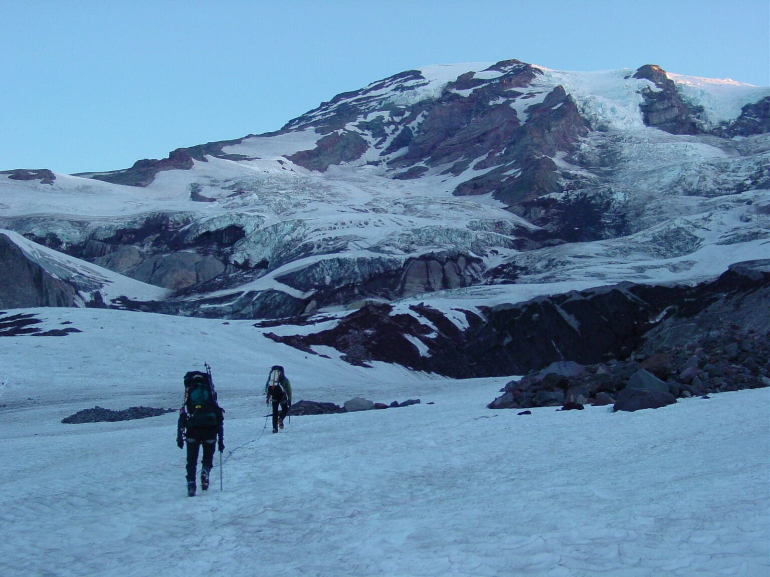A guided party trudges their way up Mount Rainier, covered in snow.