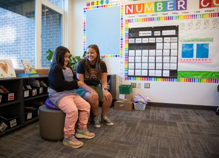 Kindergartener Claire Hagan, left, tries out a "wiggle seat" while getting a tour of her new classroom from teacher Kalli Kritsonis at Sumas Elementary on Aug. 29. The school hosted a welcome back event prior to the start of school for families and teachers to meet and reunify after months spread apart by the flooding.