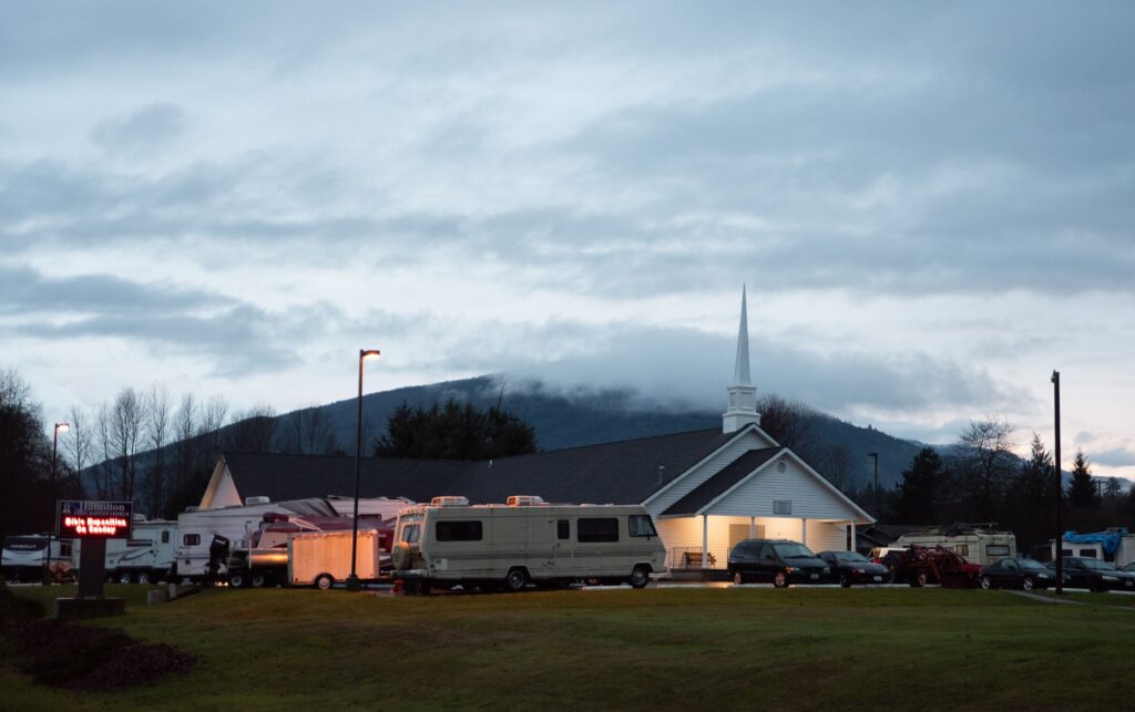 Cars and RVs fill the parking lot of Hamilton First Baptist Church early morning with the clouds covering most of the mountain behind the church.