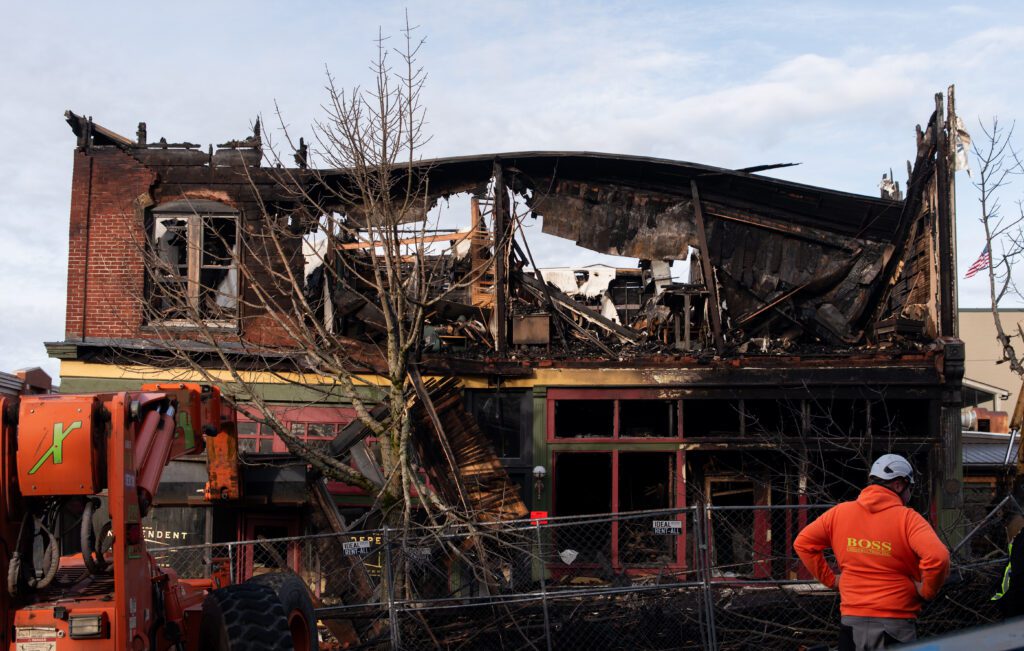 A second story building with majority of its parts burned down as a construction vehicle stands by.