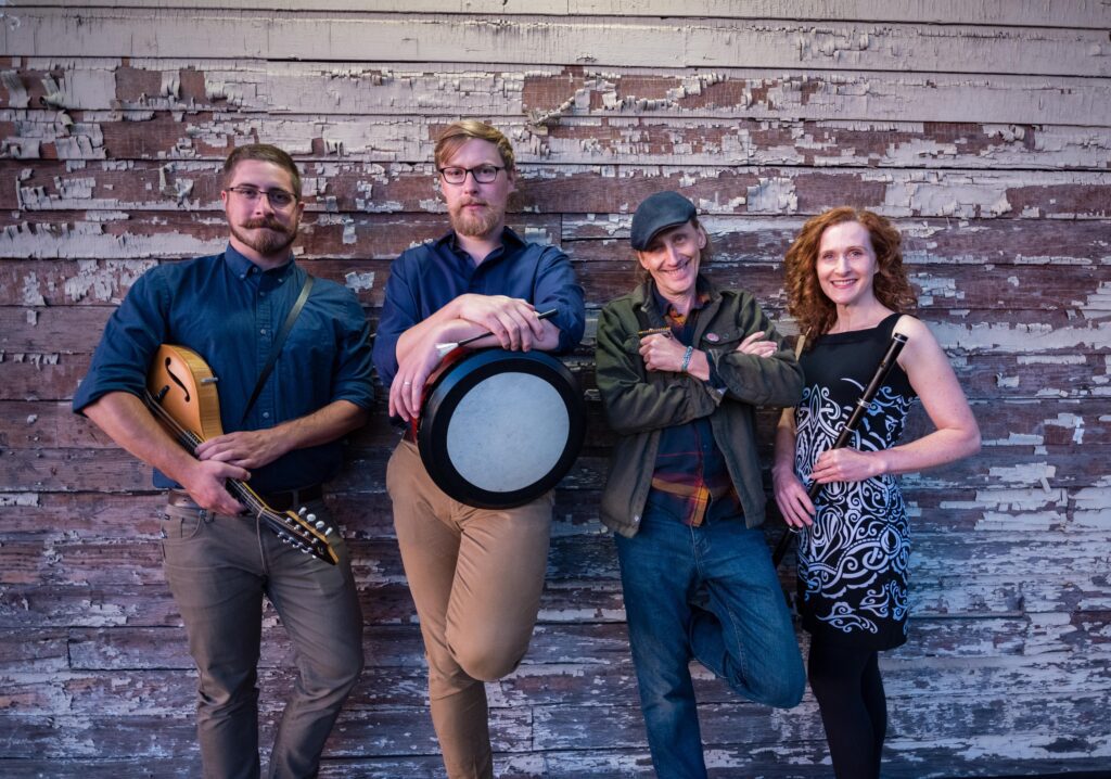 Gallowglass poses against a worn-down wall with their respective instruments.