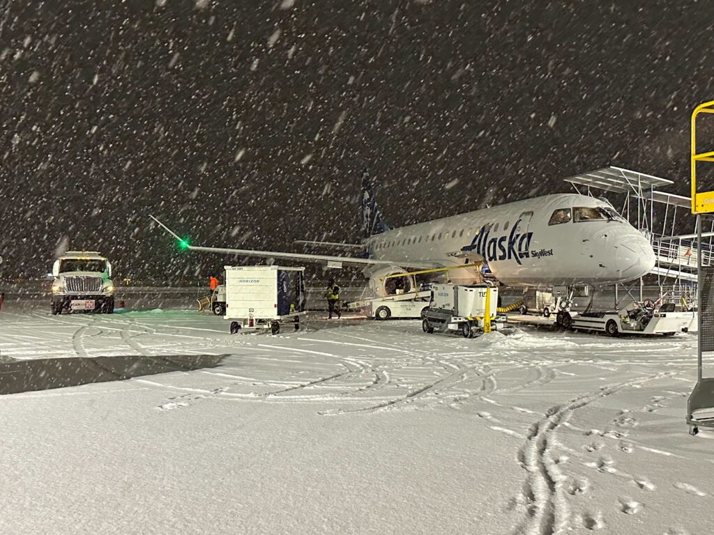 Heavy snow falls on a plane parked next to the airport as the ground is covered by snow.