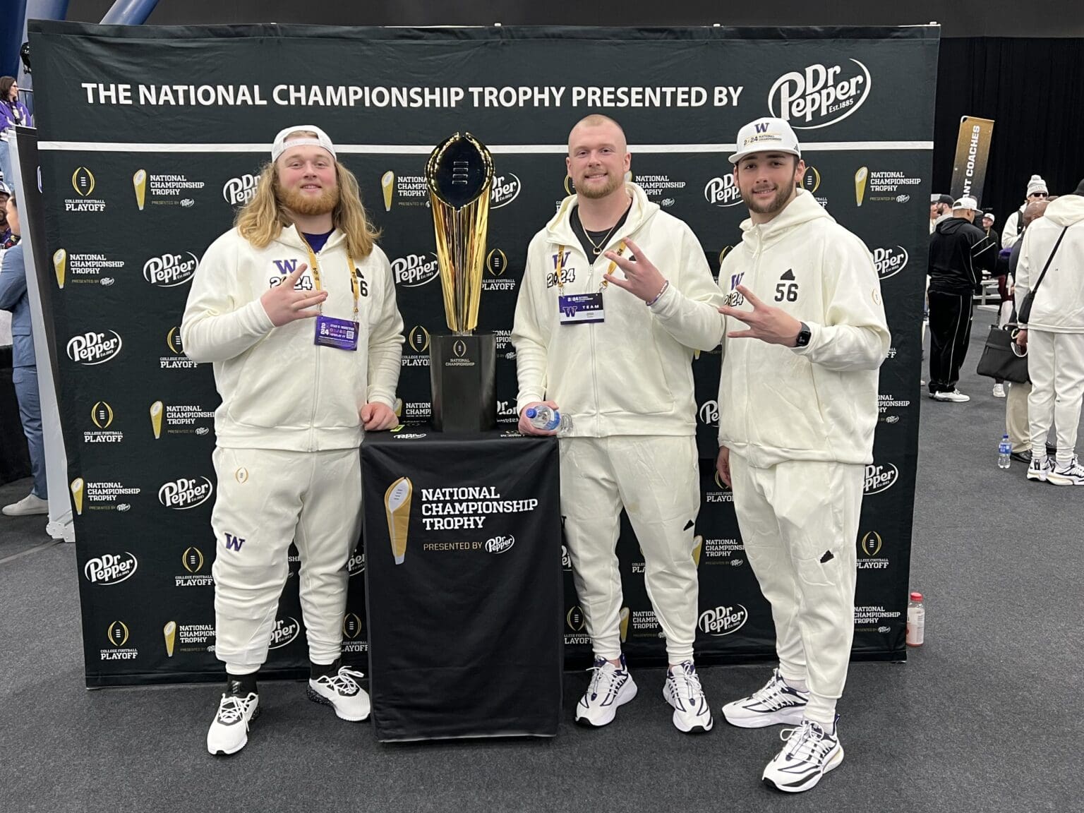 From left, Landen Hatchett, Geirean Hatchett and Jake Mason pose with the CFP National Championship trophy, all wearing white from head to toe.