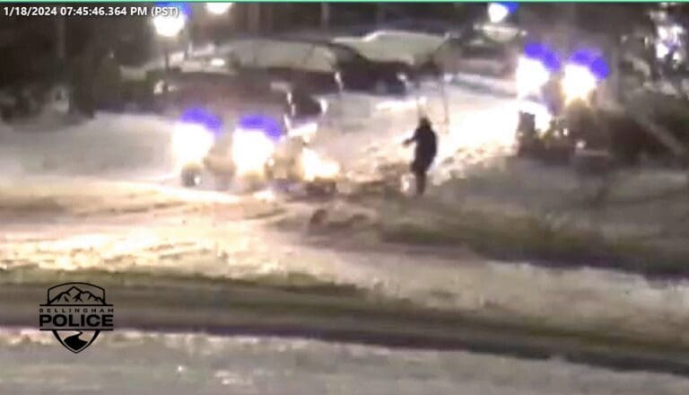 A blurry photo of a shooter walking next to cars in the snow.