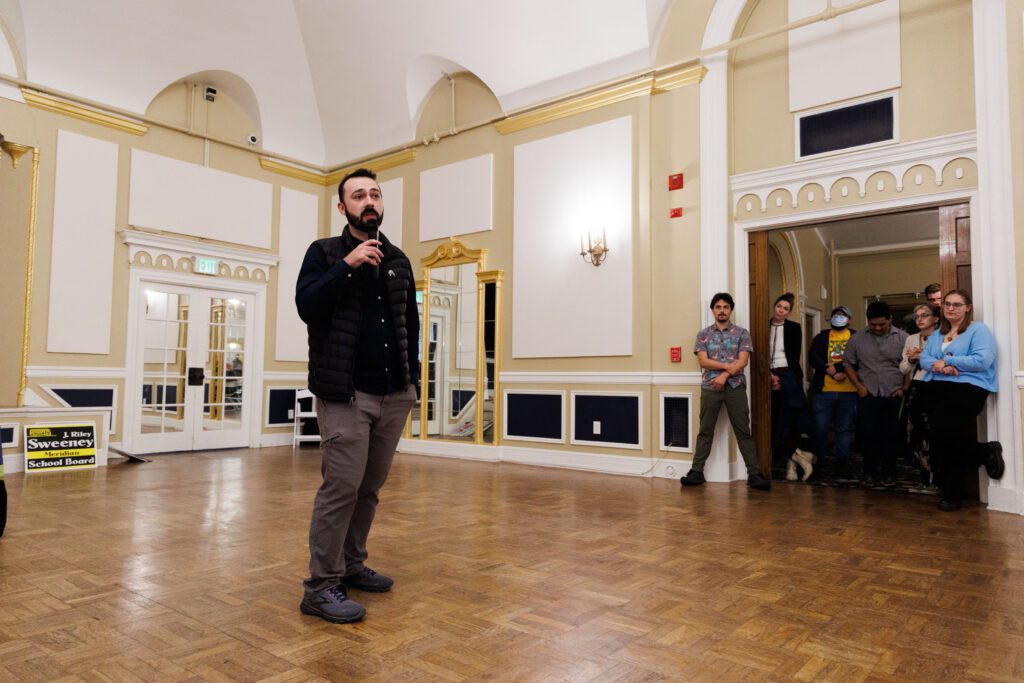 Bellingham City Council candidate Jace Cotton speaks to supporters with a microphone as more attendees listen by the doorway.