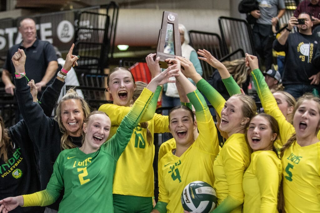 Lynden team players celebrate as they hold up the trophy above the crowded huddle.