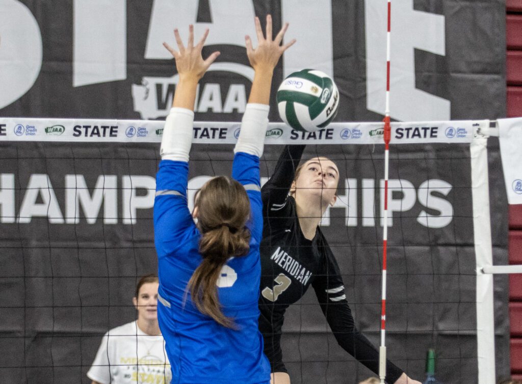 Meridian's Emry Claeys tips it over the net as an opposing member tries to block it from the other side of the net.