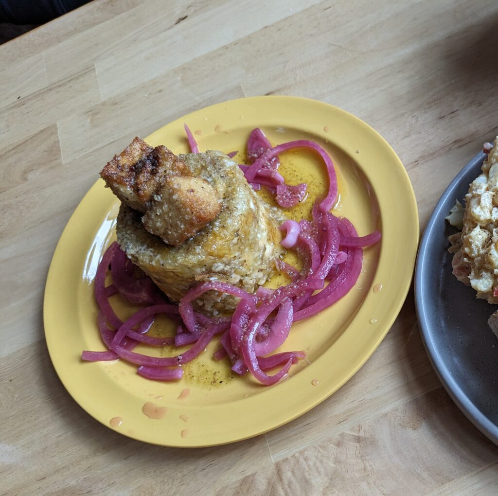 Mofongo. a savory dish of chicken cracklings, pounded plantain, and pickled red onions is served on a bright yellow plate.