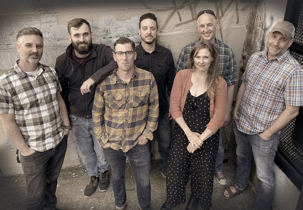 A sandy photo of local country/folk rockers North Country Highway poses for a photo with a white wall behind them.