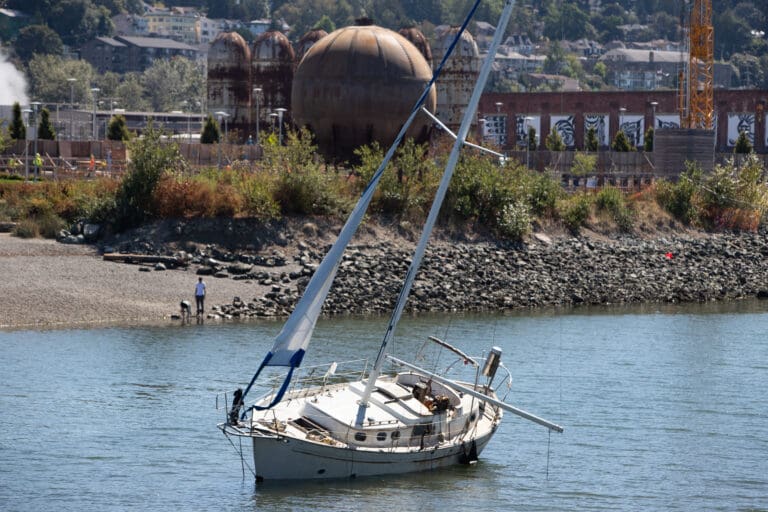 The wrecked sailboat sits in the Whatcom Creek channel in front of the rusty Acid Ball and other rusty relics of industry.
