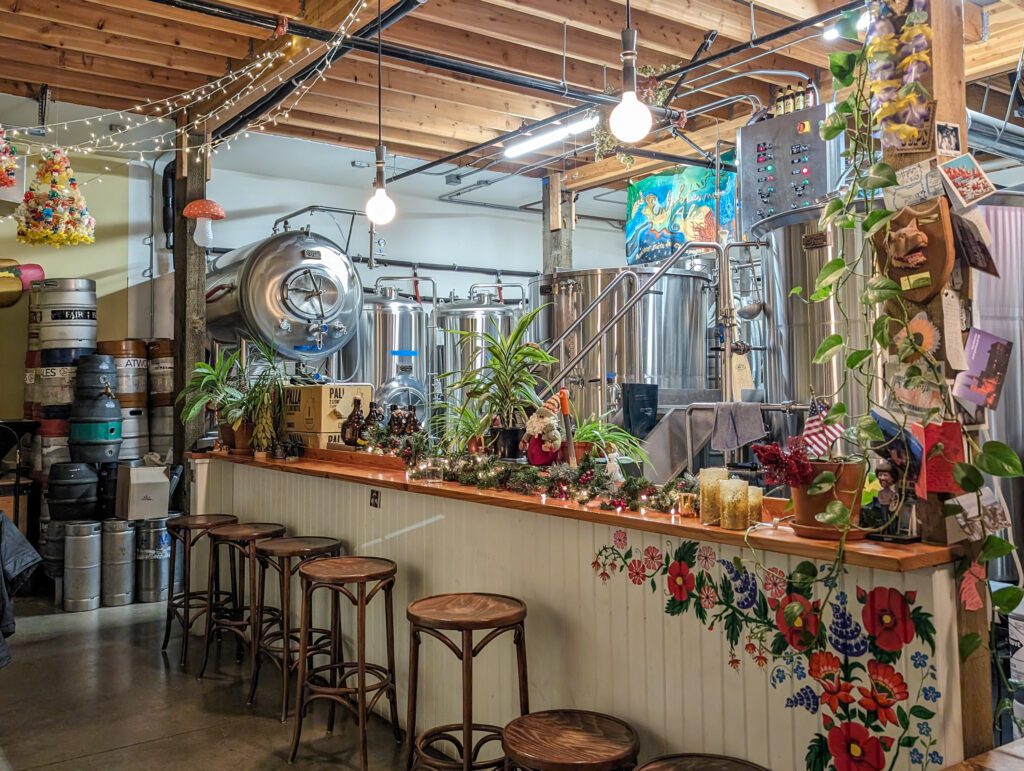 A bar counter with many stools lined up against the decorated wall has many decorations ranging from christmas lights to potted plants.