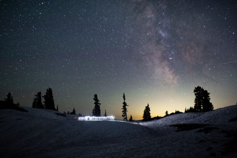 Two people move across a snowfield at Artist Point beneath the Milky Way.