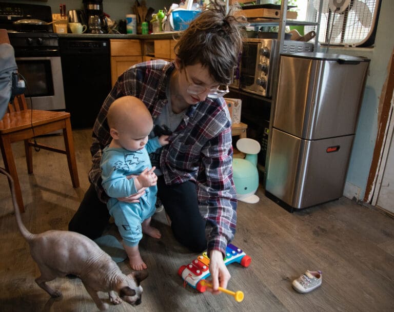 Laura Simonton amuses 10-month-old Ember with a toy Feb. 2 in their kitchen. Simonton quit her job to take care of her child.
