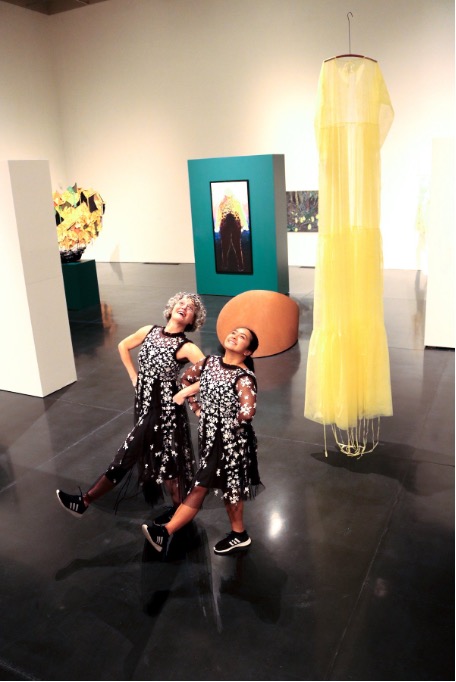 Western Washington University dance faculty Pam Kuntz and Angela Sebastian dance in a gallery with their hands to their hips, dressed in sparkly black dresses.