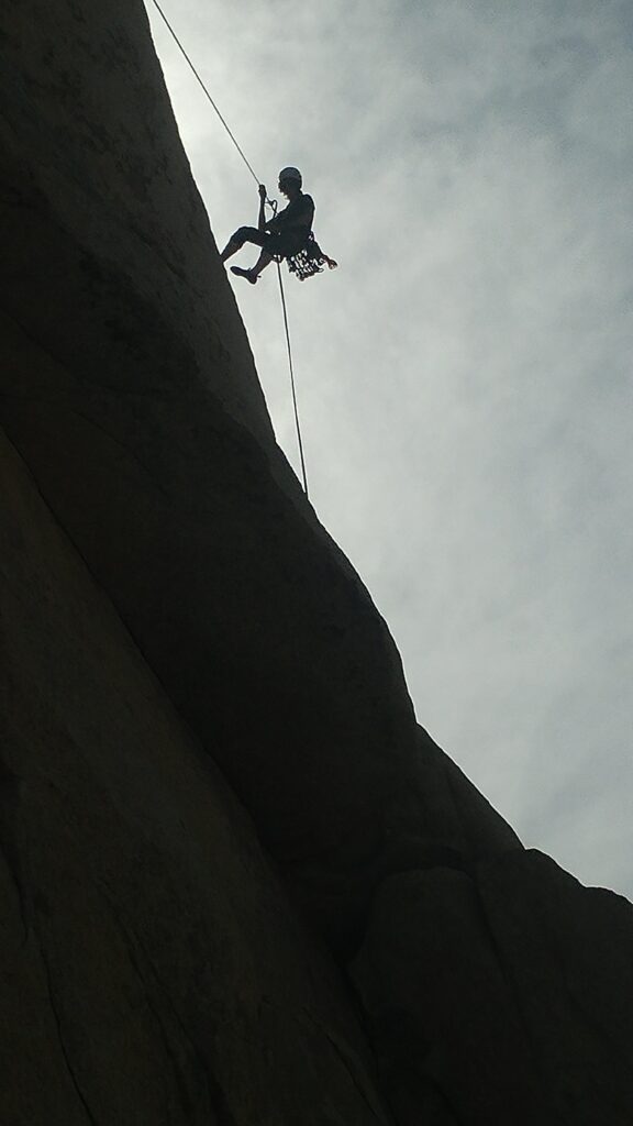 A climber's silhouette rappels off a cliff with the help of their climbing rope.