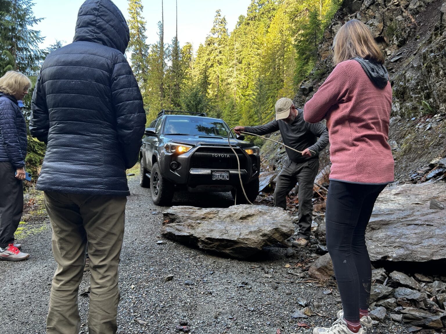 The group watches Vernon Brown of Bellingham fasten a rope to a fallen rock to the hood of the car.