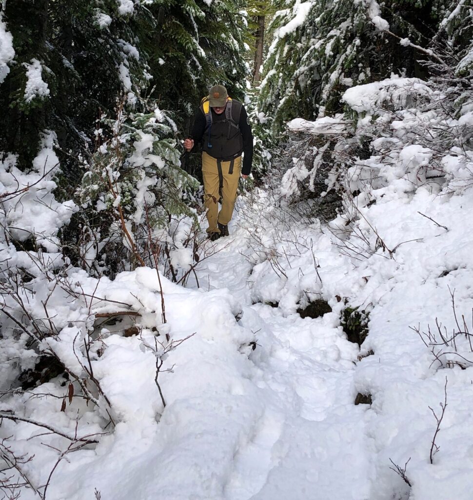 Elliott Almond carefully walks through the narrow path covered in snow and surrounded by trees, sticks, and bushes.