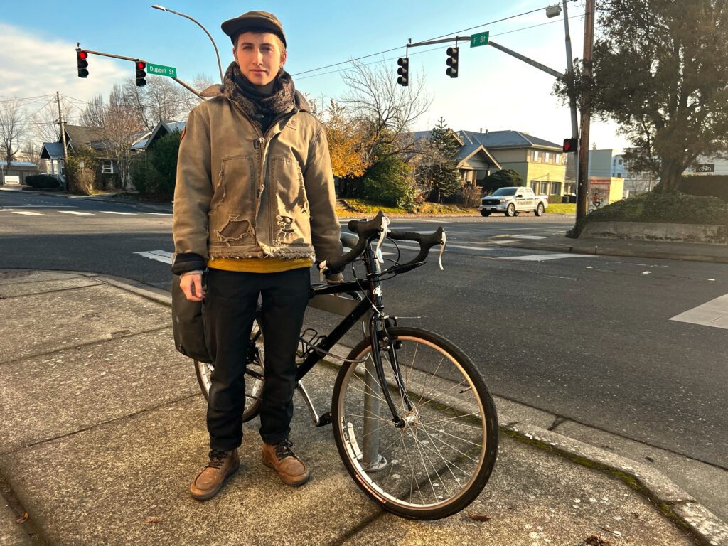 Kai Wians standing next to their bike on the sidewalk of a street.