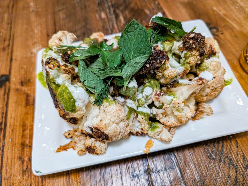 The roasted cauliflower appetizer served on a white plate and drizzled with zhug and yogurt with mint leaves.