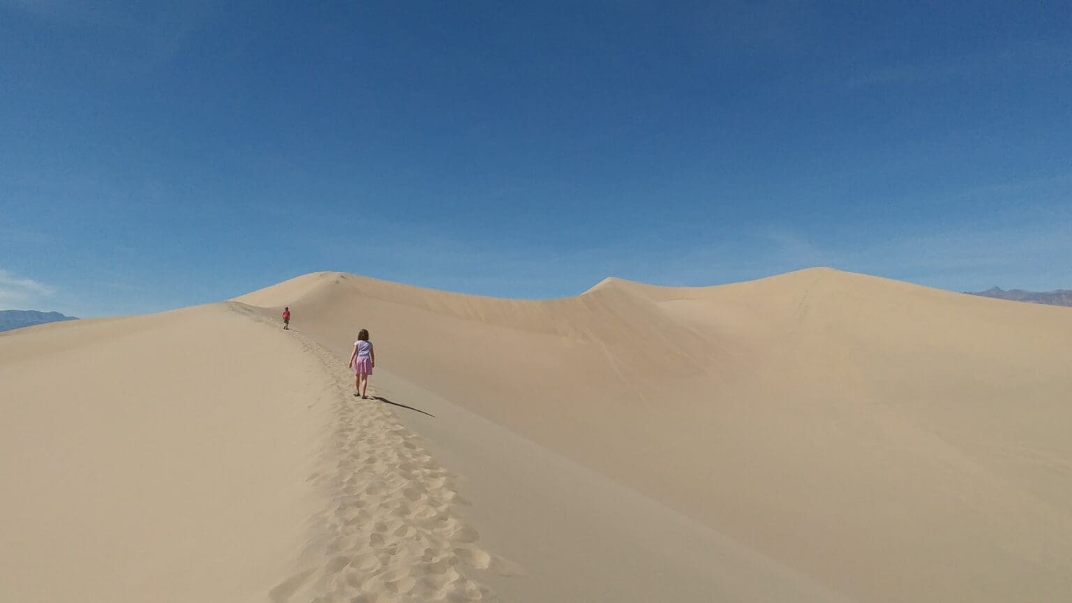 Holly and Caden Martin hike along the sand dune with the bright blue sky above them.