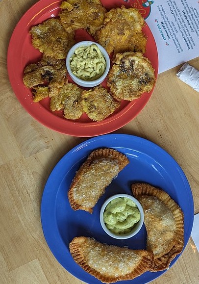 Empanadas and tostones served on a red and blue plate with a dipping sauce in the middle of each dish.