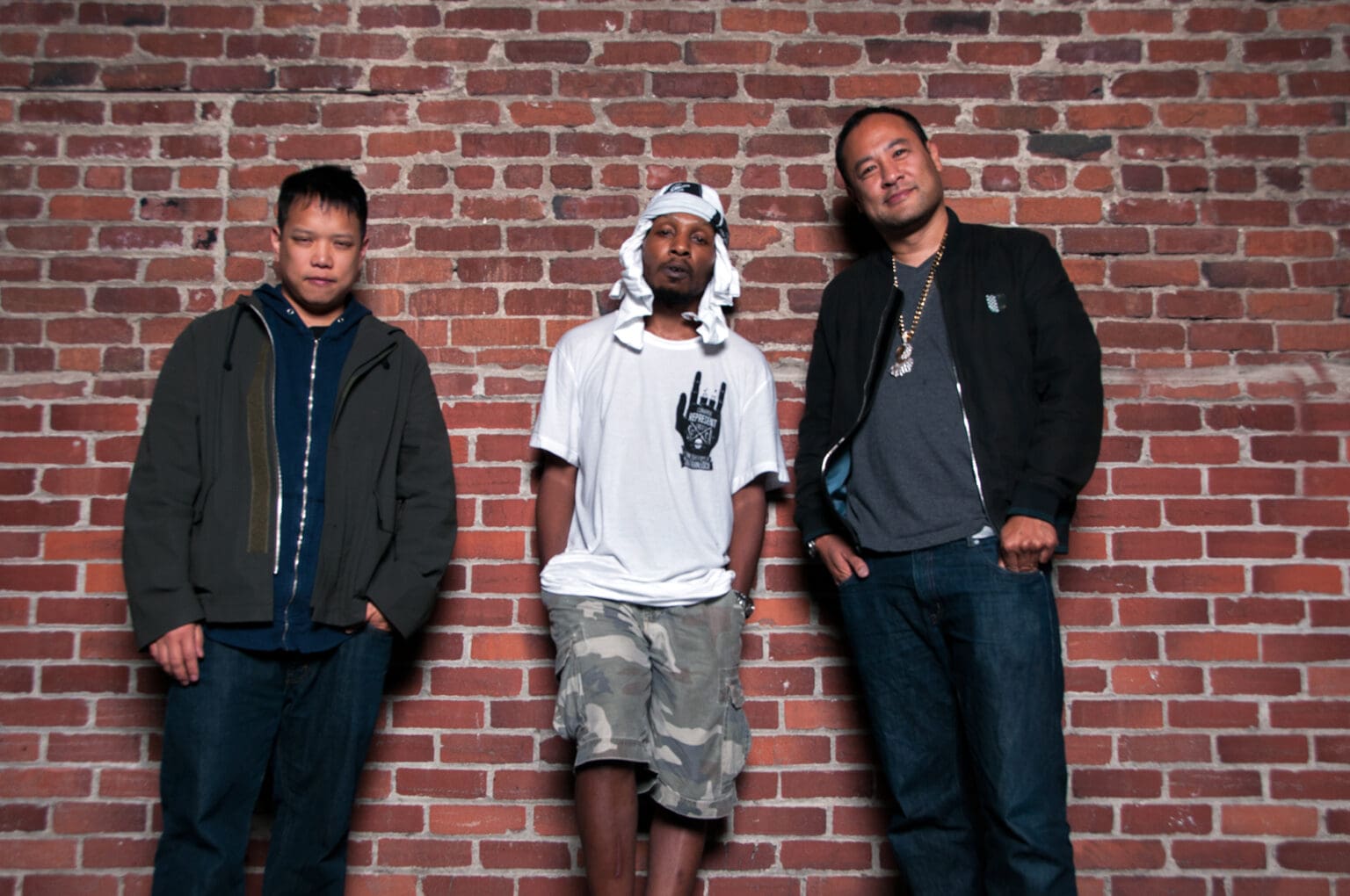 Hip-hop trio Deltron 3030 poses against the brick wall.