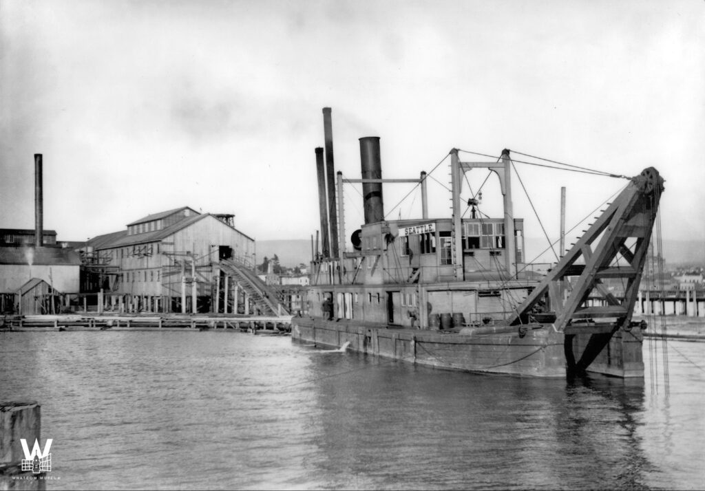 Vintage black and white photo of a dredger in the waters of Whatcom Creek Waterway.