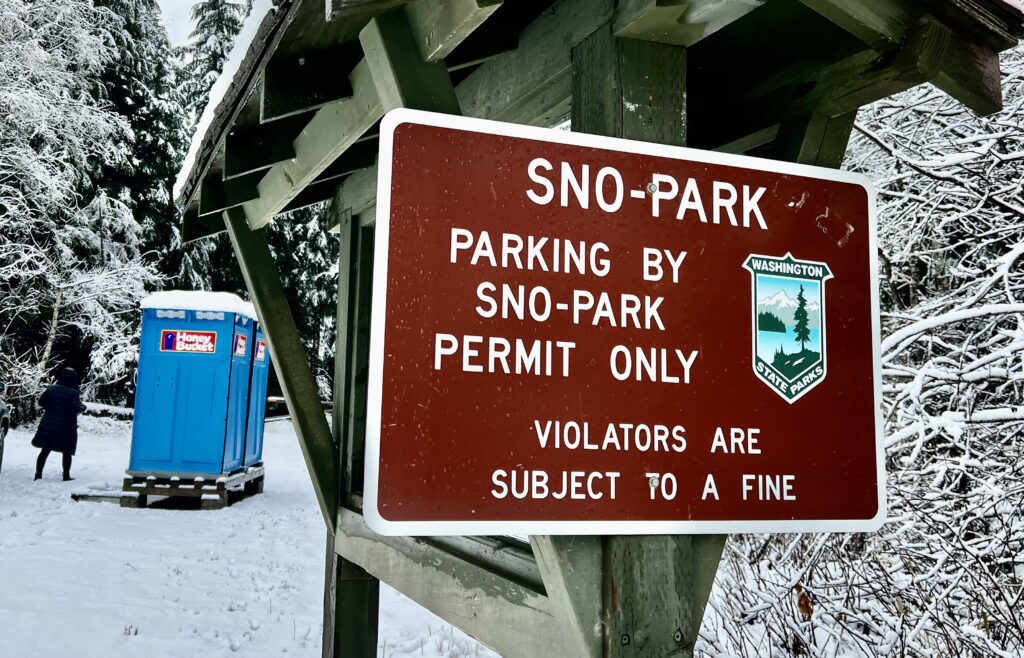 A red sign bolted on a wooden board at Washington’s Sno-Parks lets the visitor know parking by permit only and warns visitors of violating the rules.