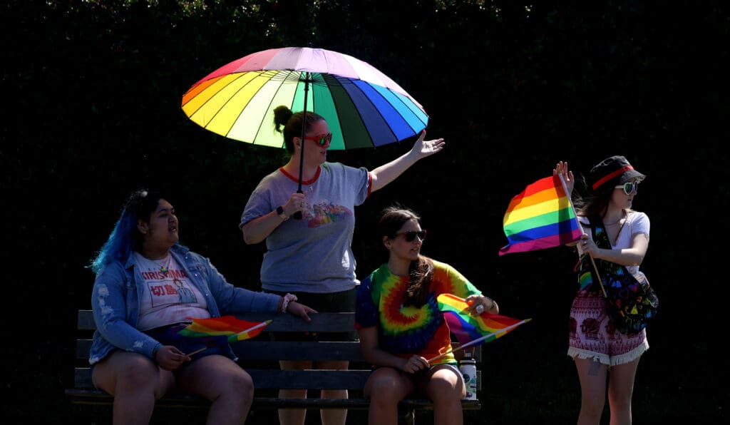 Supporters await the start of the Whatcom Youth Pride Parade along Cornwall Avenue, all waving pride flags and umbrellas.