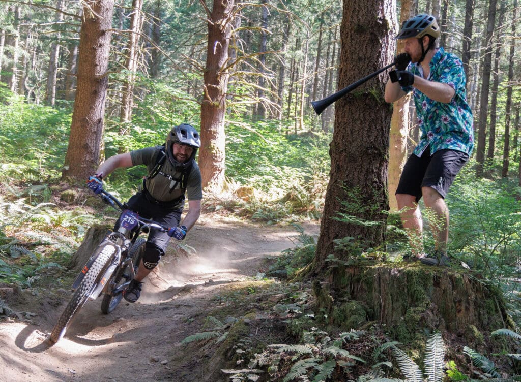 Dallan Pickard blows a vuvuzela and rings a cow bell as racers go by in the Galbraith Mountain Enduro races during the Northwest Tune-Up Festival on July 15