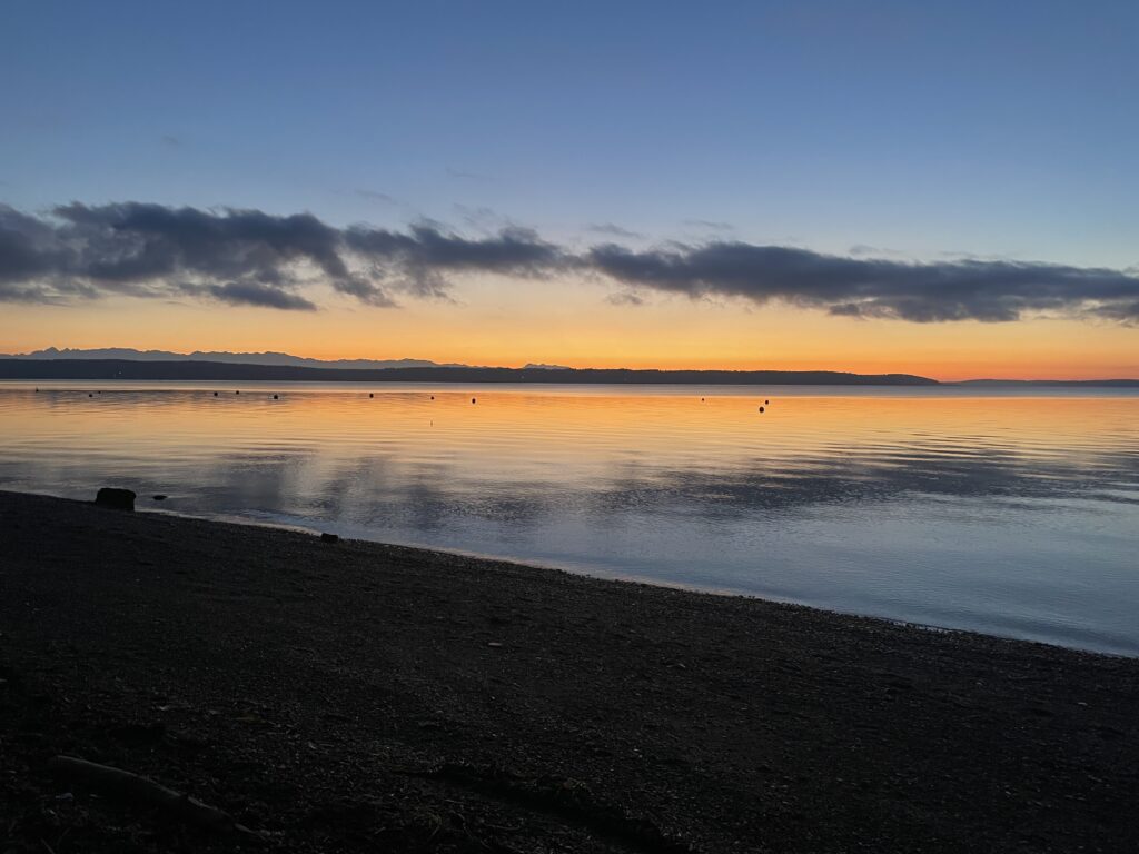 Camano Island facing Whidbey Island as the sun sets paints the water and sky orange.