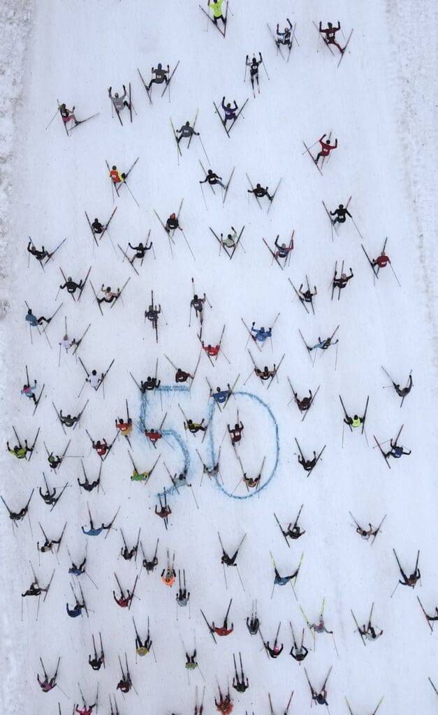 Dozens of skiers are seen on a mountain from a drone photograph.