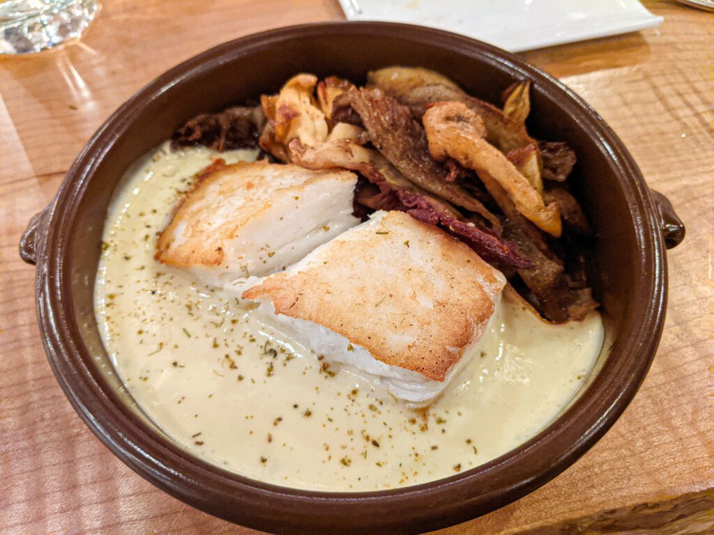Local halibut served with mushrooms, smoked béarnaise and fennel pollen is served in a brown bowl.